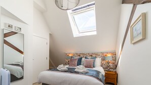 A bedroom with a large bed, a skylight, a mirror, and a nightstand.