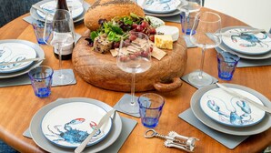 A round wooden table set for a meal with plates, glasses, and a bottle of wine.