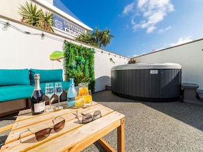 A rooftop terrace with a teal sofa, a wooden table with drinks and glasses, a hot tub, and a wall with greenery and a sign for a cinema. - Wonderful private villa for 6 guests with hot tub, WIFI, TV, patio and pets allowed (Newquay)