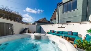 A hot tub in a backyard with a teal sofa and a shark mural on the wall.