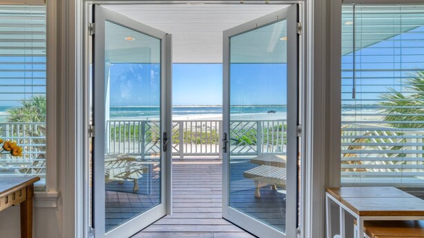 Une vue à travers une porte vitrée donnant sur une terrasse en bois avec vue sur la plage.