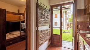 A room with a bunk bed, a decorative wall panel, a door leading to an outdoor area, and a kitchen area. - Flats With Garden in Courmayeur (Verrand)