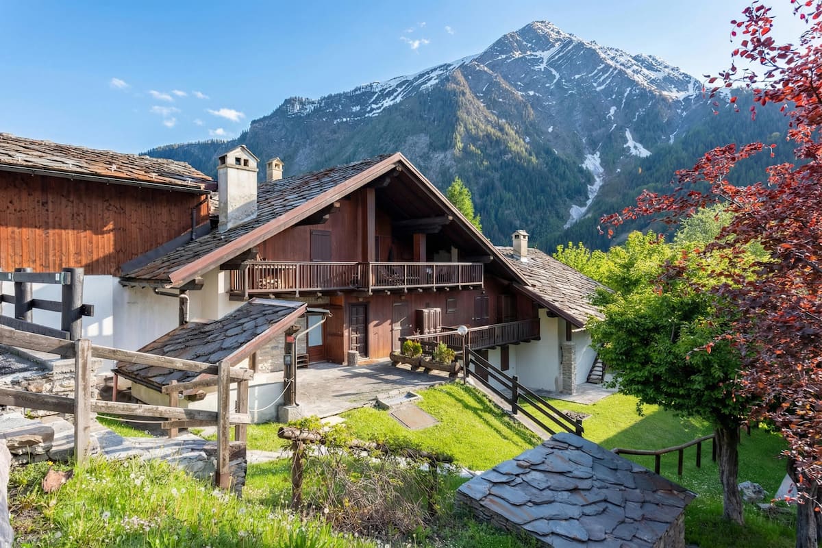 A traditional wooden chalet with a balcony, set against a backdrop of mountains.