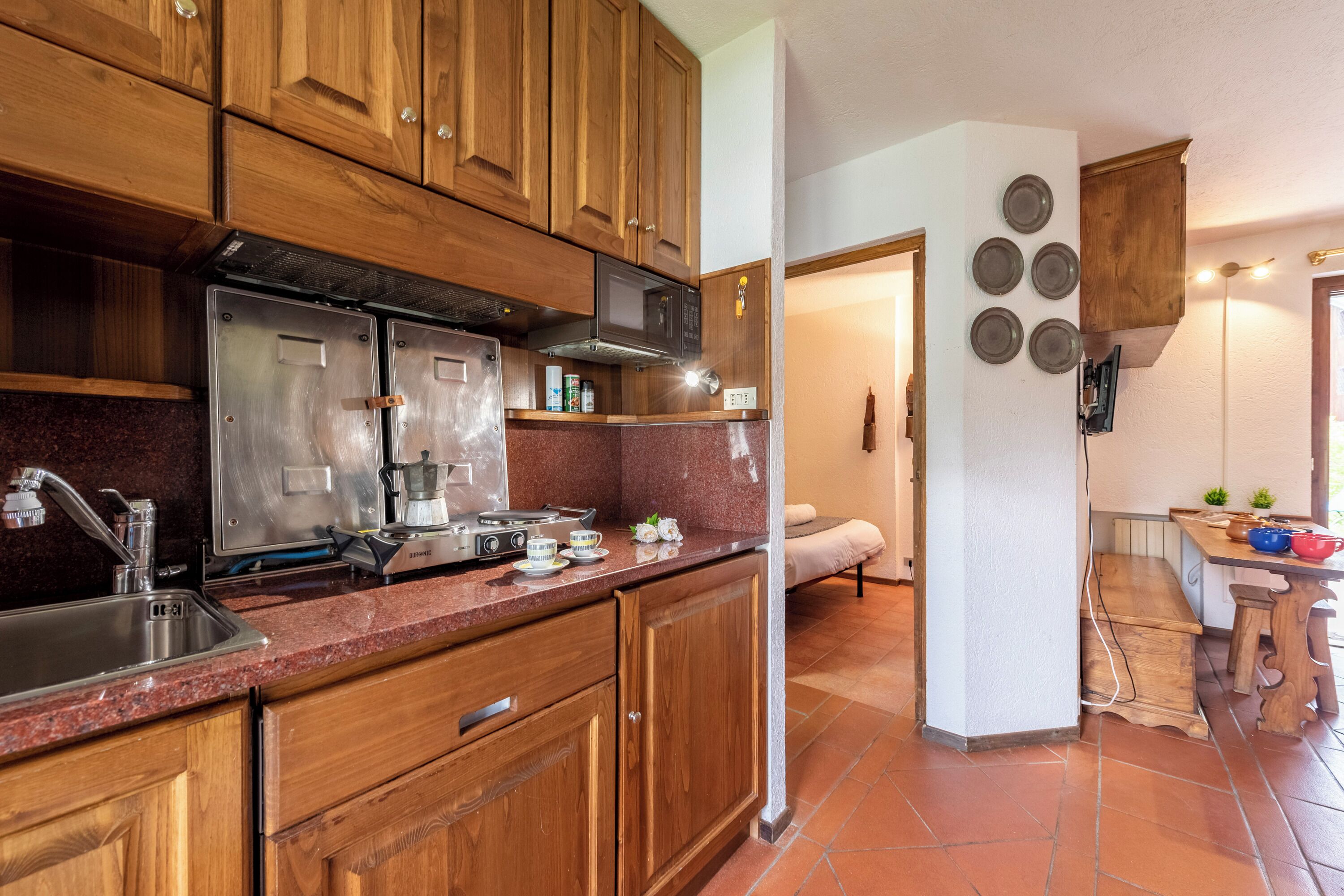 Cucina con mobili in legno, elettrodomestici in acciaio inossidabile, piano di lavoro in granito e angolo pranzo con una panca e un tavolo.