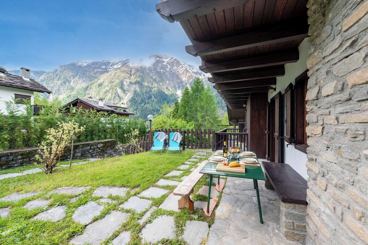 A stone building with a wooden porch, a stone pathway, and a table set for dining.
