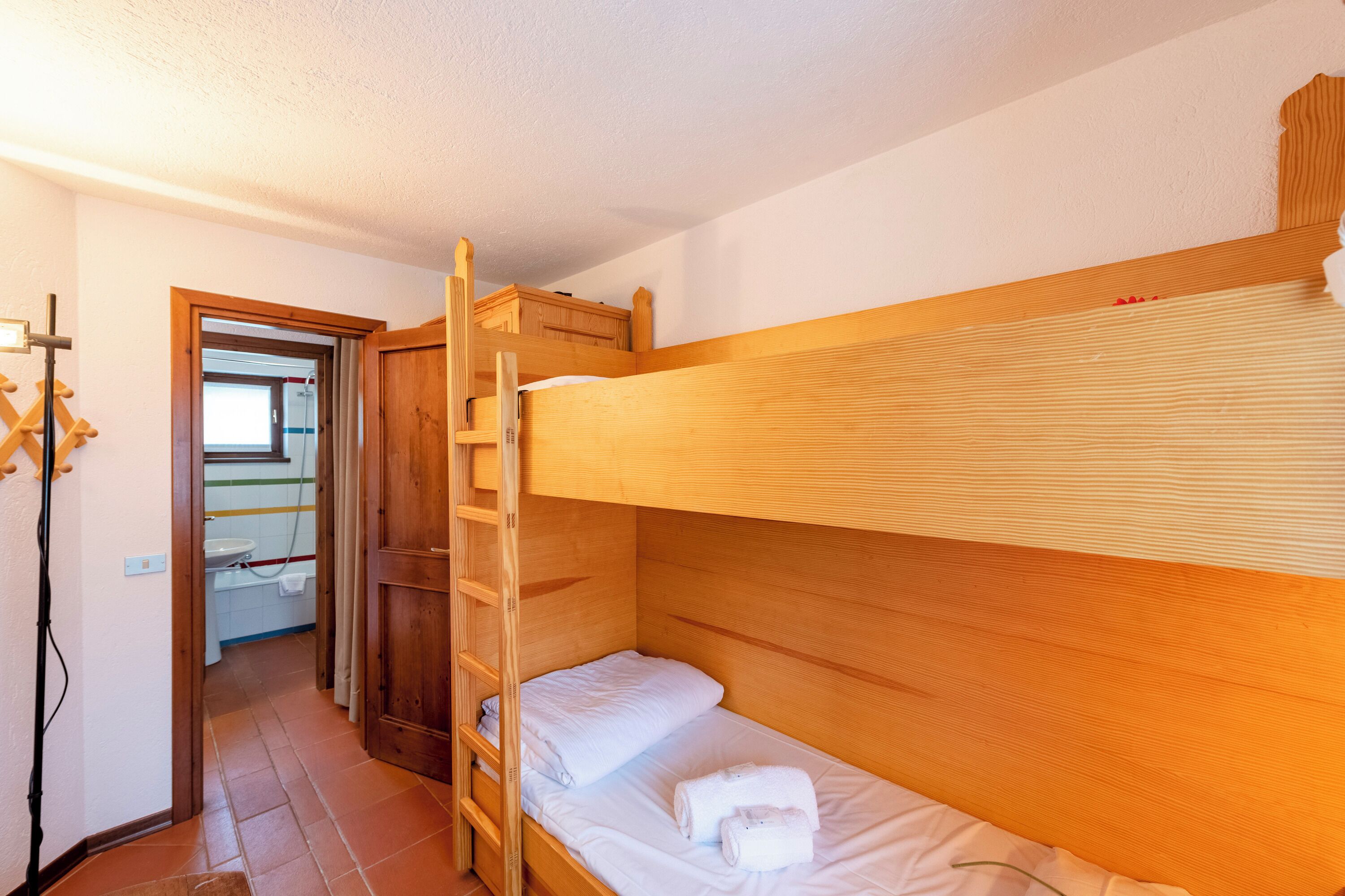 Een slaapkamer met een stapelbed, een houten trapje, een wit matras en een klein houten kastje boven het bed.