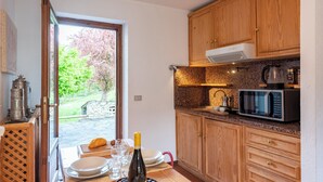 A kitchen with wooden cabinets, a microwave, and a dining area with a table set for two. - Flats With Garden in Courmayeur (Verrand)