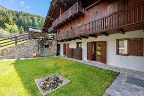 Un edificio de madera de dos pisos con base de piedra, un hogar de piedra y una escalera de piedra que lleva a una terraza de madera.