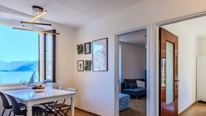 Uma zona de refeições moderna com vista para o mar, uma mesa de jantar com cadeiras e uma sala de estar acolhedora com um sofá e almofadas.