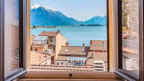 Vista da janela com um lago, montanhas ao fundo e edifícios com telhados de cerâmica em primeiro plano.