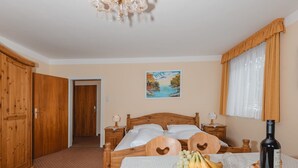 Une chambre avec un lit en bois, un tableau au mur, une fenêtre avec des rideaux et une table sur laquelle se trouvent une bouteille et des fruits.