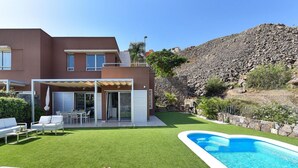 A modern house with a swimming pool, a patio with lounge chairs, and a well-maintained lawn.