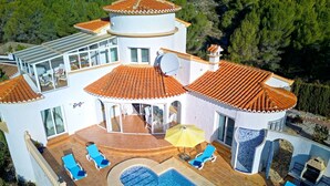 En modern villa med en swimmingpool, flera balkonger och utomhusområden med sittplatser.
