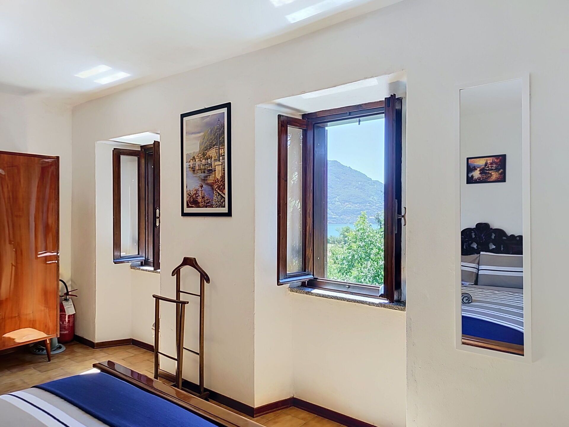 Une pièce avec un lit, une fenêtre donnant sur une montagne, un tableau encadré au mur et une porte.
