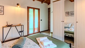 Un dormitorio con cama, una mesita de noche con lámpara, techo de madera y una puerta que da a otra habitación.