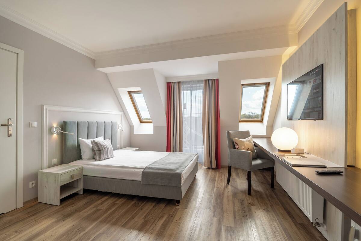 Une chambre moderne avec un lit, un bureau et une chaise. Il y a des fenêtres et une vue sur l’extérieur.