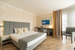 Una habitación de hotel con una cama grande, un escritorio, una silla y un televisor en la pared.