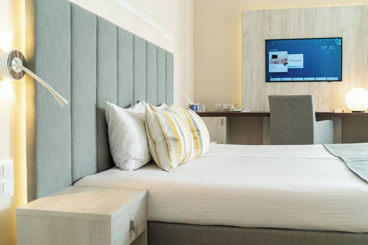 Une chambre d’hôtel comprenant un lit, une table de chevet, une lampe, une télévision et un bureau avec une chaise.