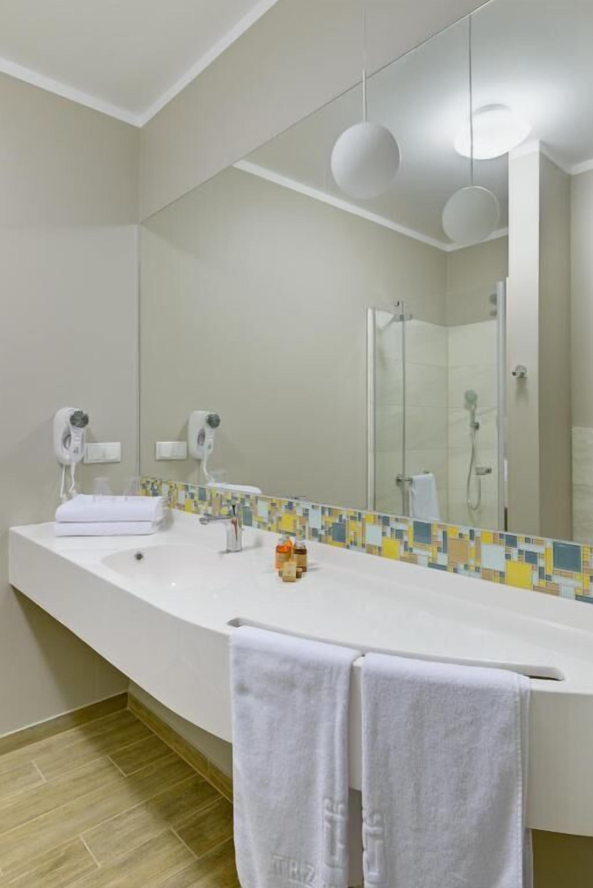 Un baño moderno con un espejo grande, lavamanos blanco y dos secadores de pelo.