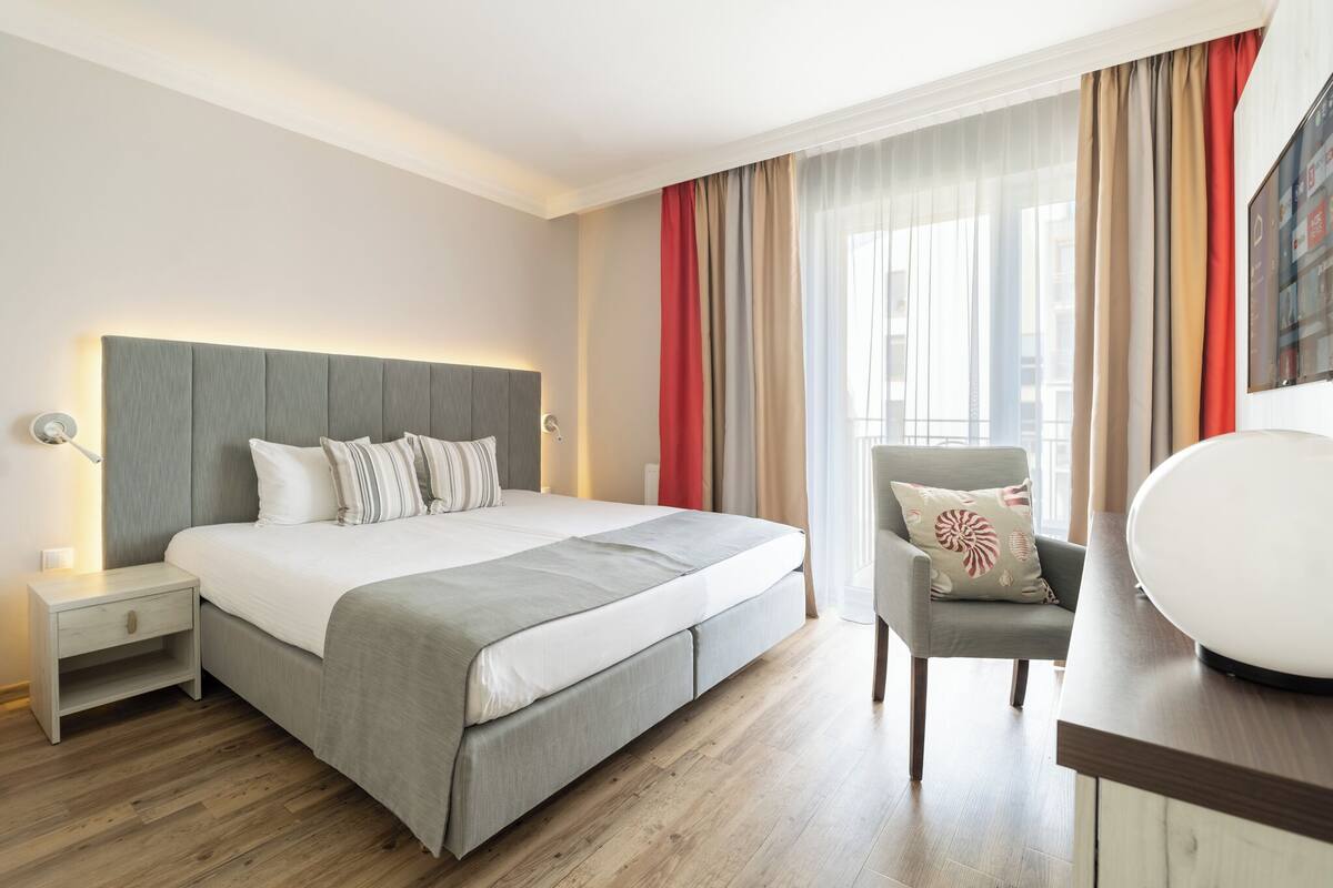 Une chambre d’hôtel moderne, dotée d’un grand lit, d’une table de chevet, d’une chaise et d’un bureau avec une lampe.