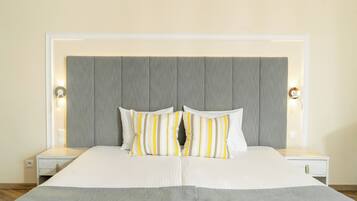 A neatly made bed with a grey headboard, two bedside tables with lamps, and a white wall.