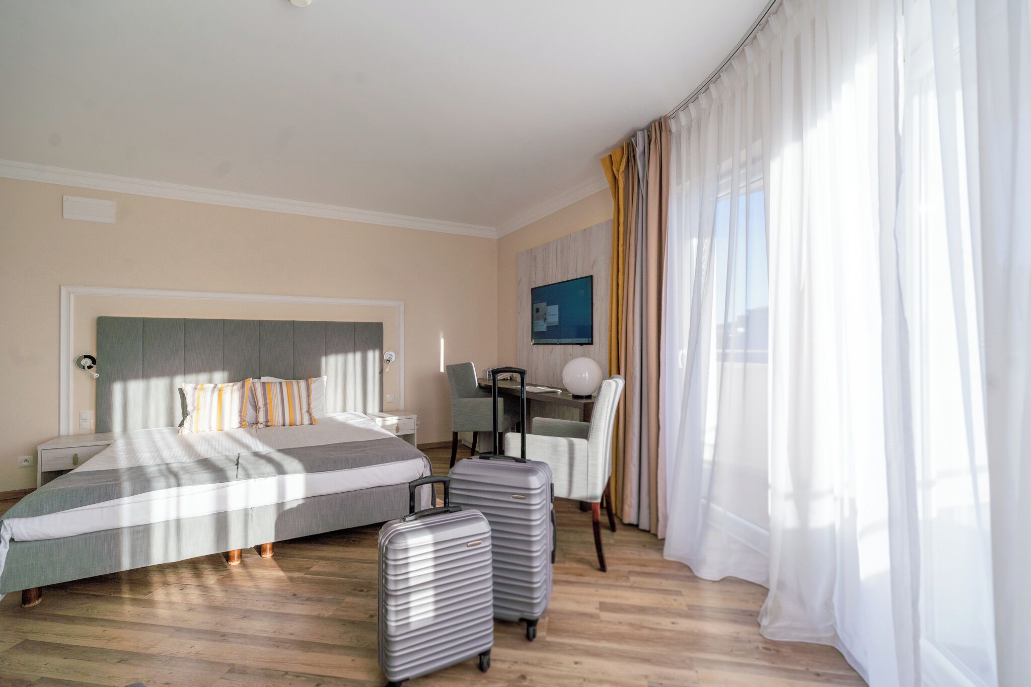 A hotel room with a bed, a desk, a chair, and two suitcases.