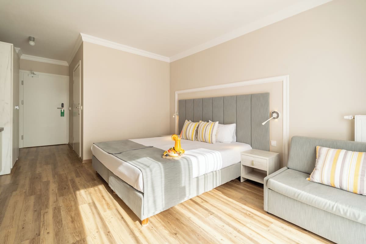 Une chambre d’hôtel moderne avec un grand lit, une table de chevet, un canapé et un plancher en bois.