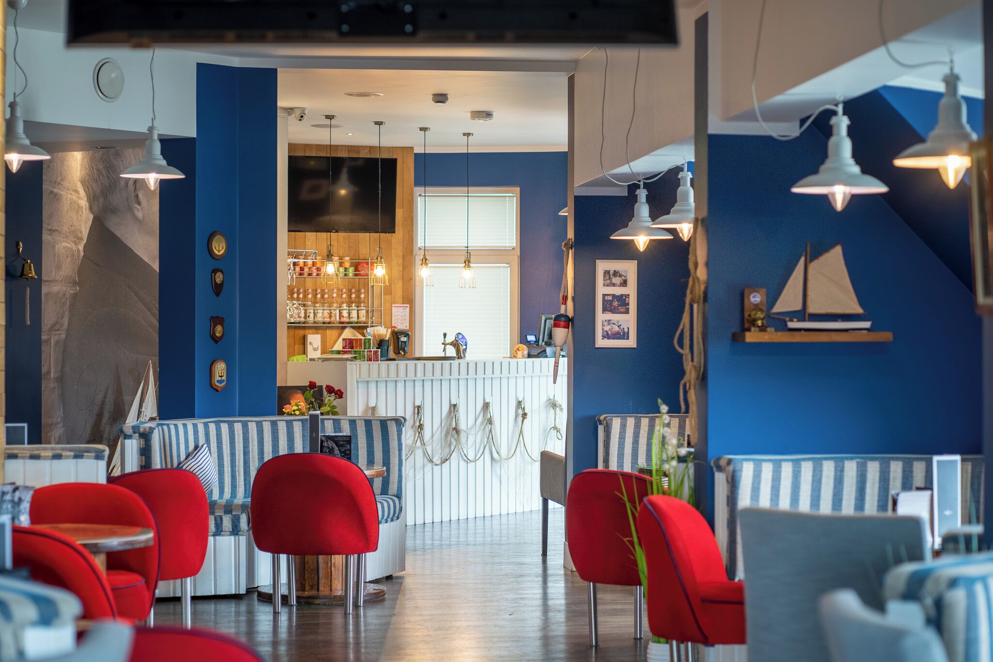 Un restaurante con asientos rojos y azules, una zona de bar y decoración mural con temática náutica.