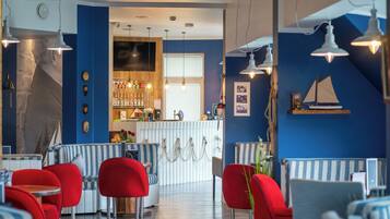 Un restaurante con asientos rojos y azules, una zona de bar y decoración mural con temática náutica.