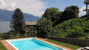 Une piscine rectangulaire à l’eau d’un bleu limpide, bordée d’une margelle en briques, et dont le décor est composé d’une végétation luxuriante et d’un paysage montagneux.
