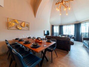 A dining area with a wooden table set for four, surrounded by blue chairs. A sofa and a television are visible in the background. - Stunning private villa for 8 guests with WIFI, hot tub, TV, patio and pets allowed (Newquay)