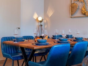 Uma mesa de jantar posta com cadeiras azuis, copos de vinho e pratos.