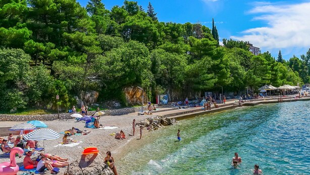 A beach with clear water, people sunbathing, and umbrellas.