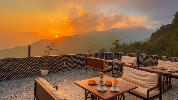 A terrace with seating and tables, a patterned wall, and a sunset view over mountains. - Hotel Rockland Residency (Dehradun)