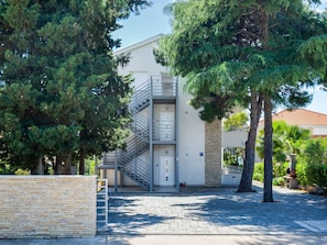 A modern building with a metal staircase leading to an entrance, surrounded by trees and a paved area.