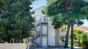 A modern building with a metal staircase leading to an entrance, surrounded by trees and a paved area. - Beautiful apartment for 6 guests with WIFI, A/C, TV and terrace (Zadar)