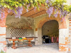 An outdoor patio with a brick archway, a wooden table with chairs, and hanging purple flowers.