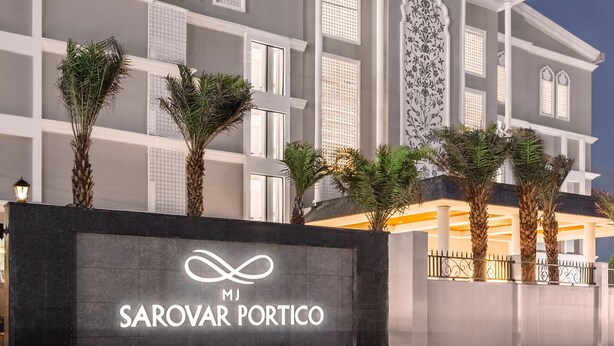 A hotel with a modern facade, palm trees in front, and a prominent sign reading "Sarovar Portico." - MJ Sarovar Portico Haridwar (Haridwar)