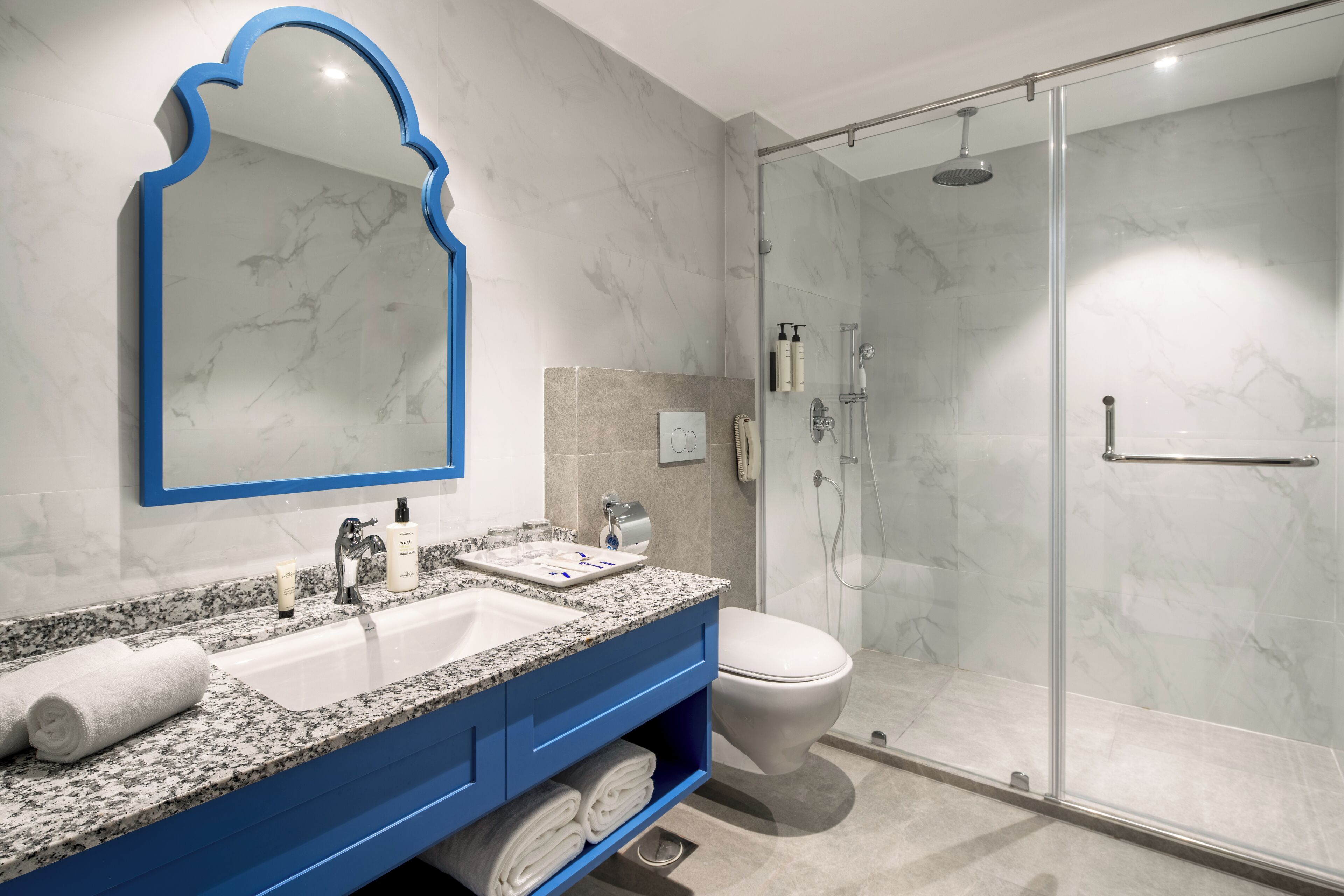 Une salle de bain moderne avec un lavabo en marbre, un meuble-lavabo bleu, une cabine de douche en verre et un grand miroir avec un cadre bleu.