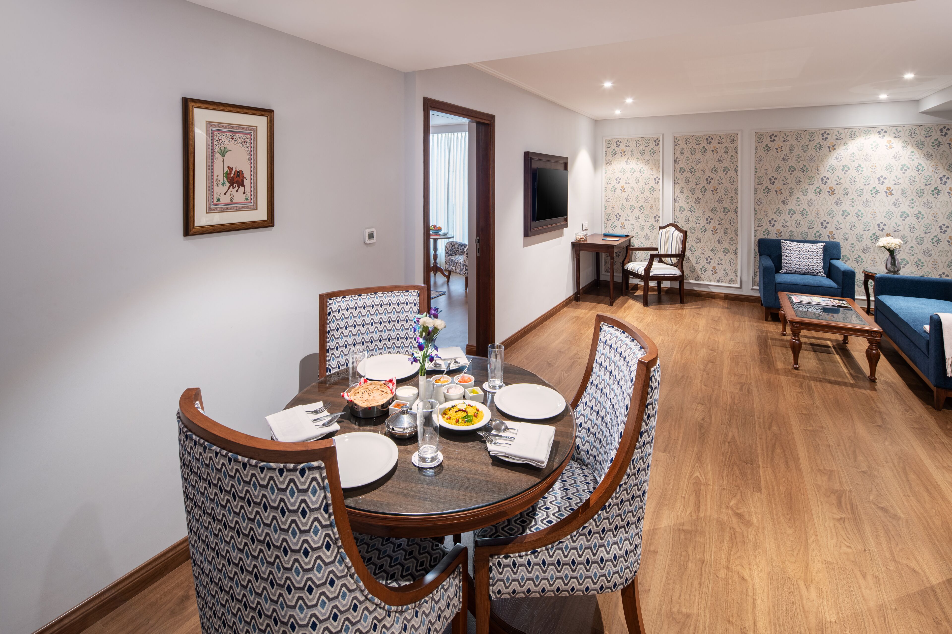 A dining area with a round table, patterned chairs, and a television in the background.