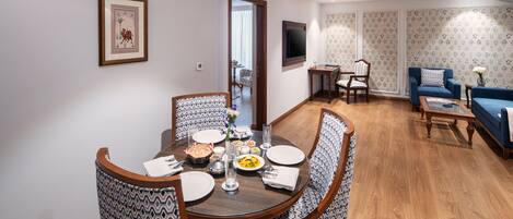 A dining area with a round table, patterned chairs, and a television in the background.