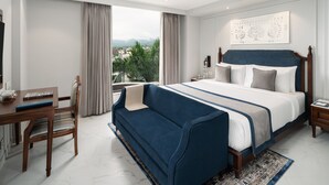 A bedroom with a large bed, a wooden desk, and a view of the outdoors. - MJ Sarovar Portico Haridwar (Haridwar)