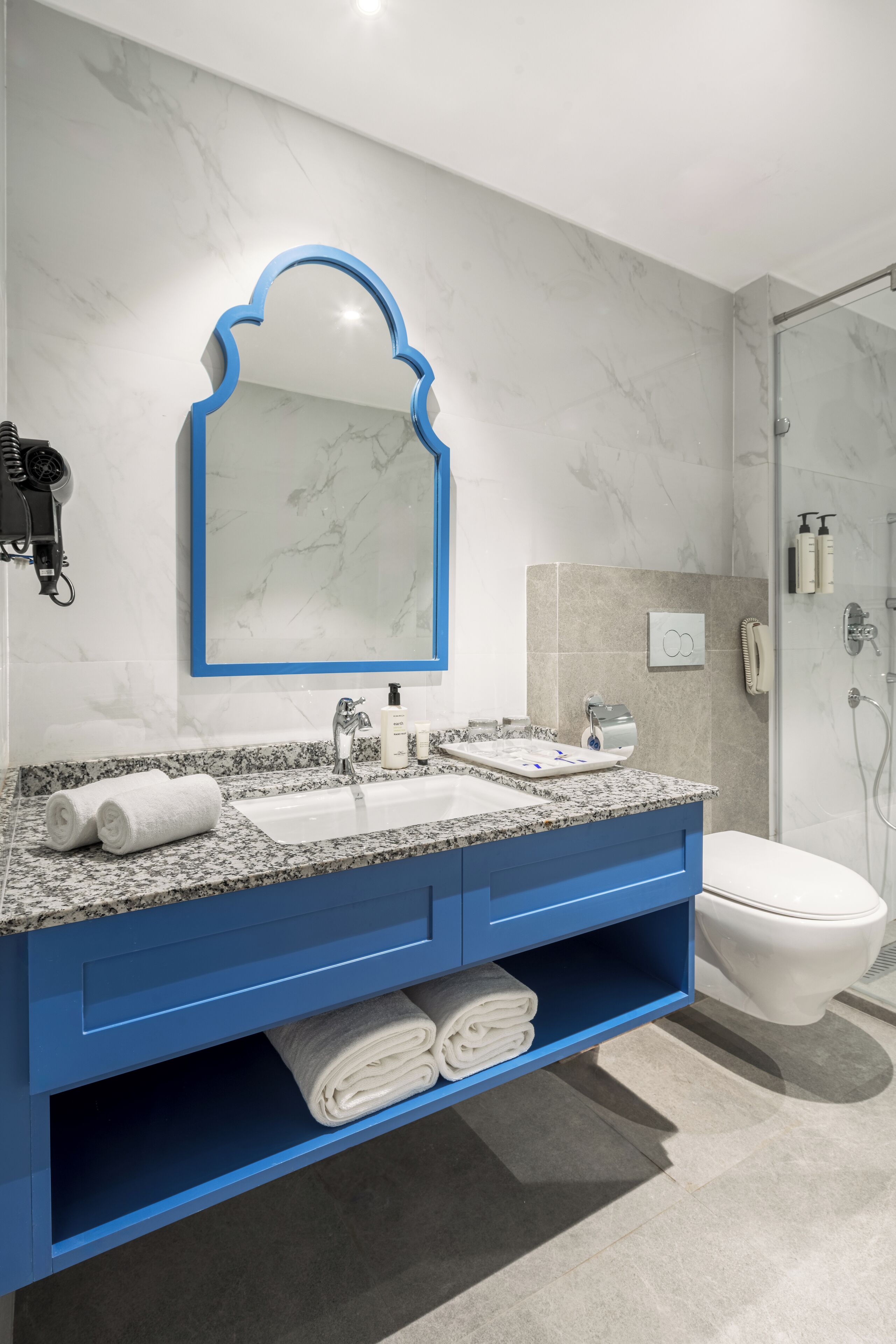 Ein modernes Badezimmer mit Marmorwaschbecken, blauer Waschtischkommode und einer Duschkabine aus Glas.