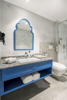 Un baño moderno con lavamanos de mármol, tocador azul y cabina de ducha con mampara de vidrio.