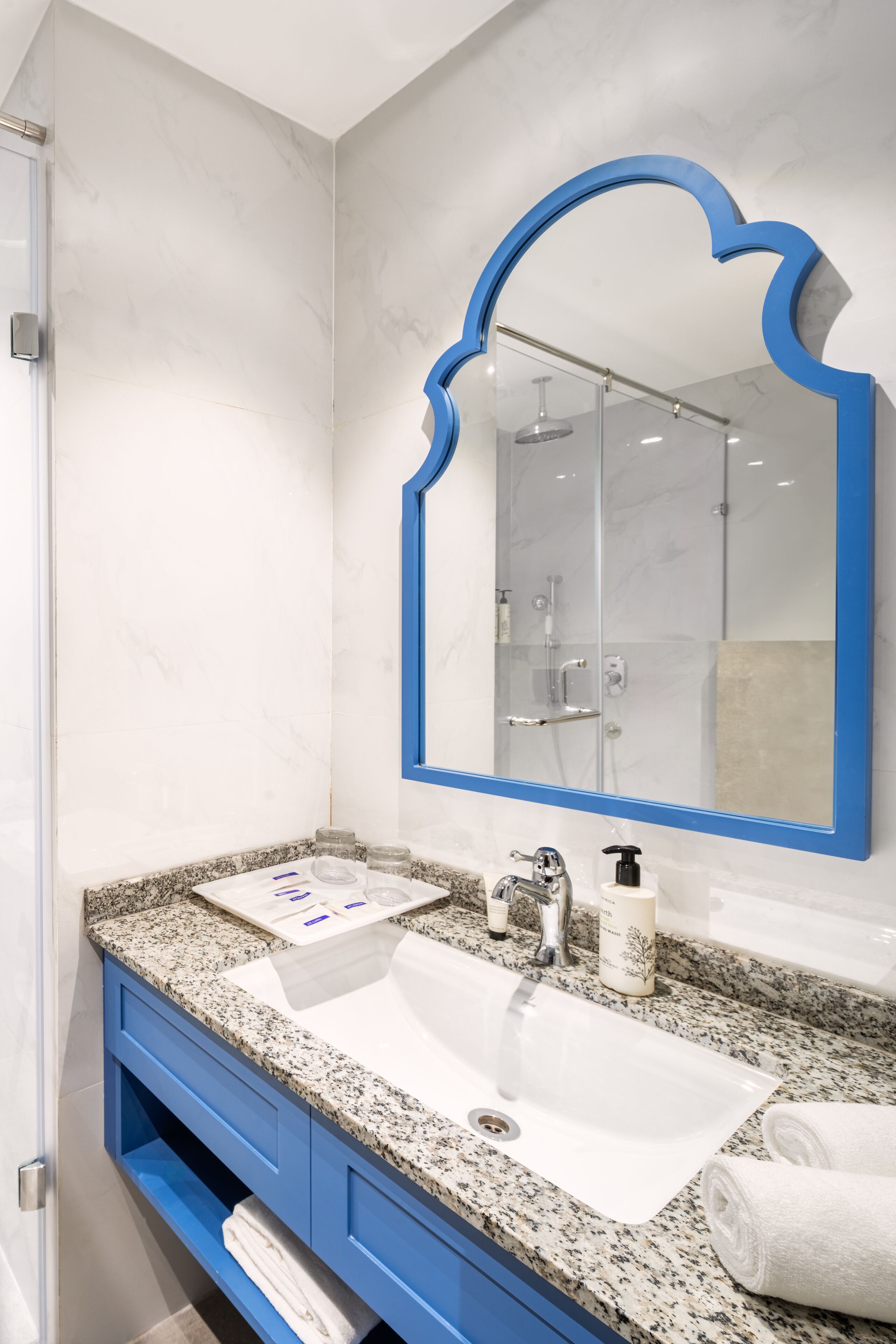 Een moderne badkamer met een witte wastafel, een blauwe badkamerkast en een grote spiegel met een blauwe lijst.