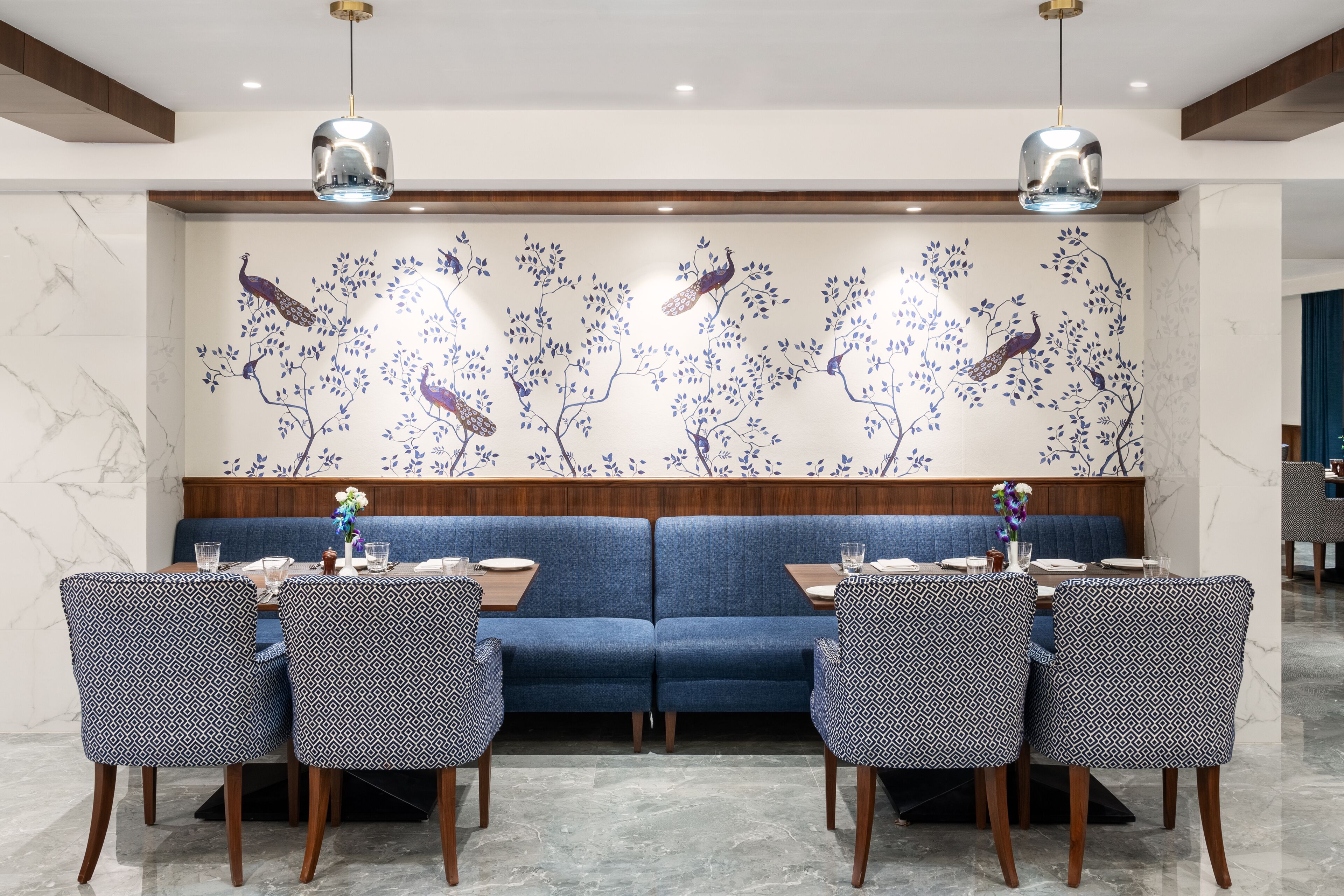 Zona pranzo con divano blu, sedie decorate e un murale con pavoni.