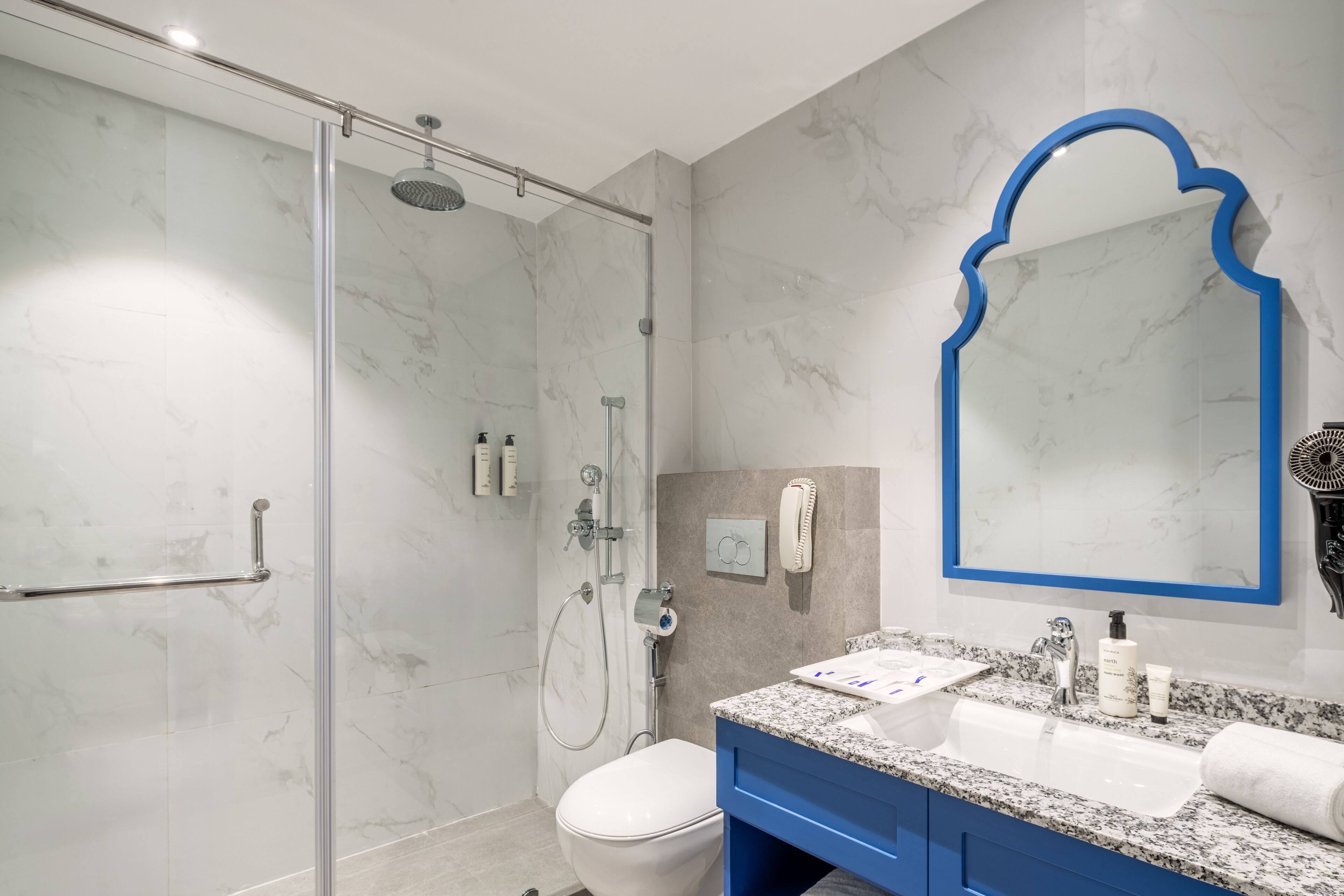 A modern bathroom with a glass-enclosed shower, a white toilet, a blue vanity with a sink, and a large mirror with a blue frame.