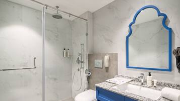 Un baño moderno con ducha acristalada, inodoro blanco, tocador azul con lavamanos y un espejo grande con marco azul.