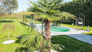 A pool area with a palm tree, a hanging chair, and a well-maintained lawn. - Lovely apartment for 4 people with pool, WIFI, TV, patio and pets allowed (Castell'alfero)