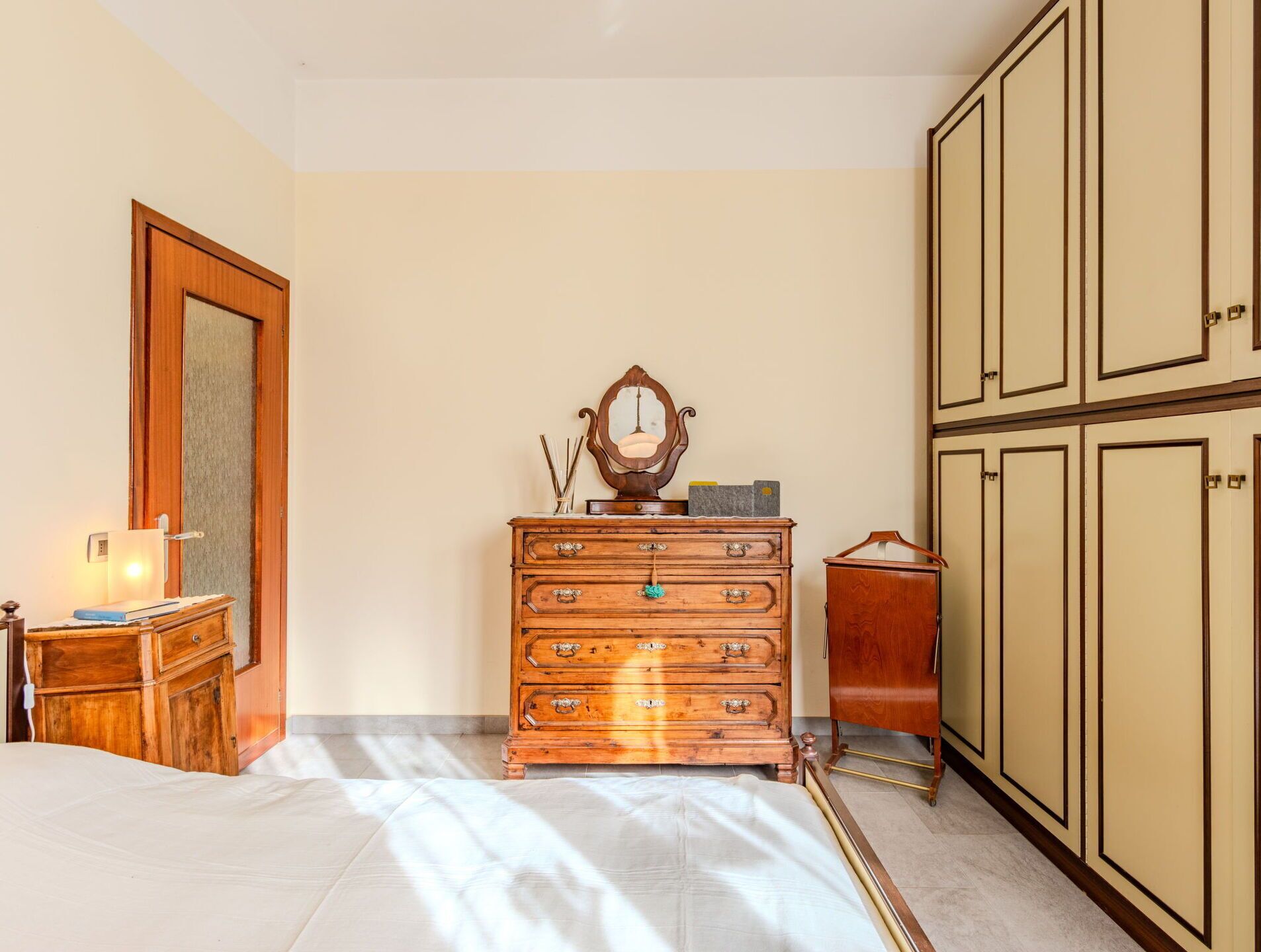 A bedroom with a wooden dresser, a bed, a mirror, and a wardrobe.
